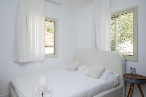 a white bedroom with a white bed with two windows at R26-Boutique in Zikhron Ya'akov