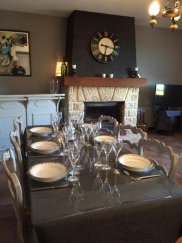 une table avec des chaises et une cheminée avec une horloge. dans l'établissement La Loge Du Vigneron, à Vauciennes