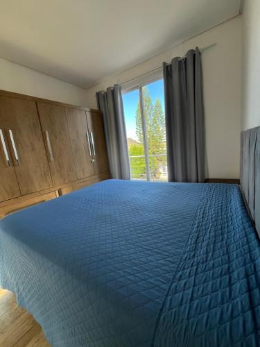 a bedroom with a blue bed with a large window at Casa com Piscina em Xangri-Lá RS in Xangri-lá