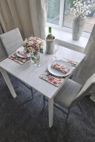 a white table with plates and glasses and flowers on it at Plum Cottage in Keswick