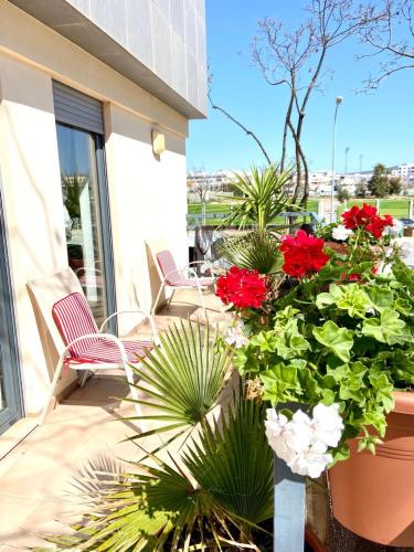 a patio with two chairs and red flowers and plants at Zenit marina village Olhao T2 appartement in Olhão
