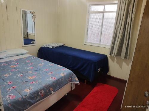 a bedroom with two beds and a window and a red rug at Casa 2 Quartos - Vila Real in Chapecó