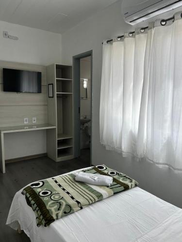 a bedroom with a bed with white sheets and a television at HL Hotel in Pelotas