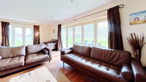 a living room with brown leather couches and windows at Meadow Shores - Part of the The Bay Filey Holiday Village with pool, gym and direct beach access, pub, restaurant, tennis and meadows walks in Filey