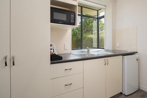 a kitchen with white cabinets and a sink and a window at ASURE Phoenix Motor Inn in Blenheim