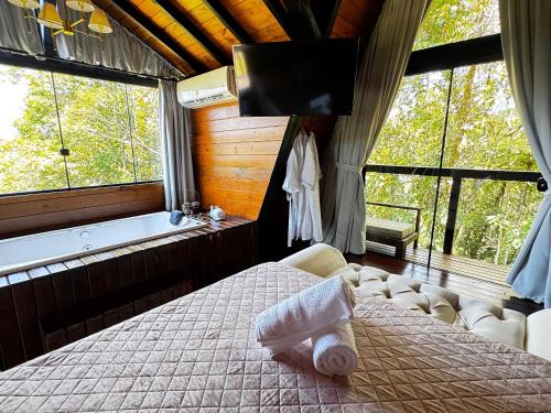 a bedroom with a bed and a tub and windows at Romantic nature retreat | Hot tub and fireplace in São Pedro de Alcântara