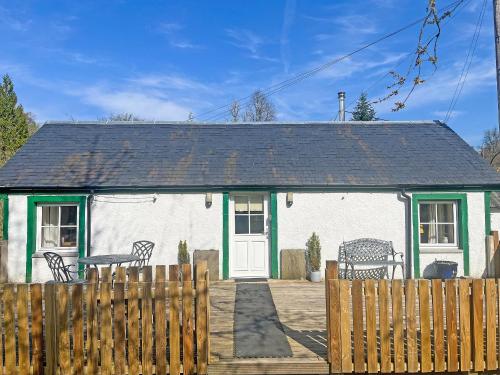 a white and green house with two benches in front of it at Bonnie's Bothy in Port of Menteith