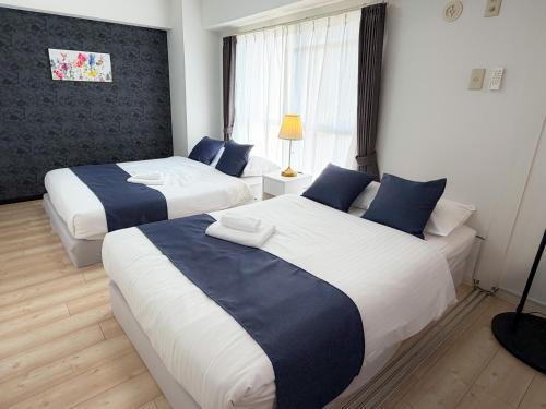 a bedroom with two beds with blue and white sheets at BALCOM STAY Hiroshima Deshio in Hiroshima