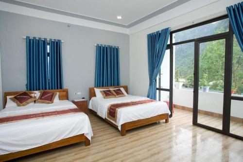 two beds in a bedroom with blue curtains at Linda Home in Phường Chày