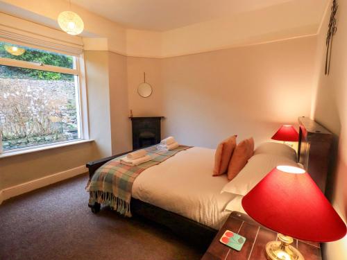 a bedroom with a bed with a red lamp and a window at Yewbarrow Cottage in Grange Over Sands
