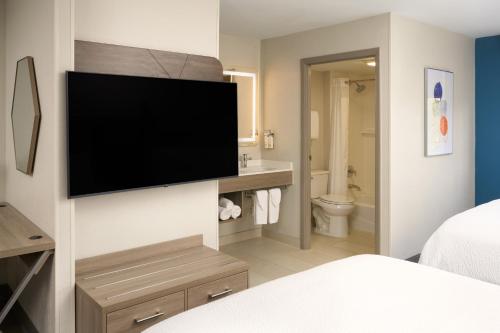 a bathroom with a television on a wall in a bedroom at Holiday Inn Express Hotel & Suites Kendall East-Miami by IHG in Kendall