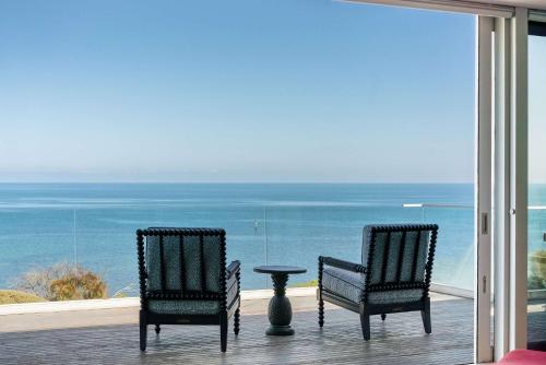 two chairs and a table on a balcony with the ocean at The Veranda - Panoramic Bay Views Private Beach Access Pool in Mount Eliza