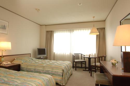a hotel room with two beds and a desk and a window at Grand Plaza Nakatsu Hotel in Nakatsu