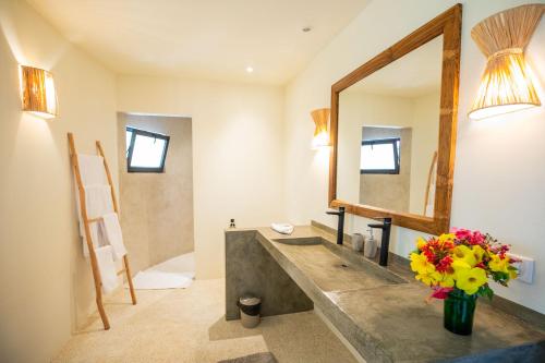a bathroom with a sink with a mirror and flowers at Adouna Bay in Cap Skirring