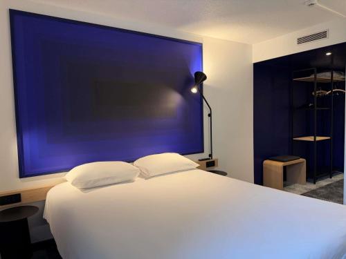 a bedroom with a large white bed with a blue wall at ibis Rennes Beaulieu in Cesson-Sévigné
