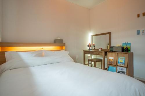 a bedroom with a white bed and a desk and a mirror at Joohane Jejudo House in Jeju