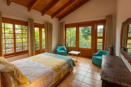 a bedroom with a bed and two chairs and windows at Casa Tropical Atitlán in Panajachel