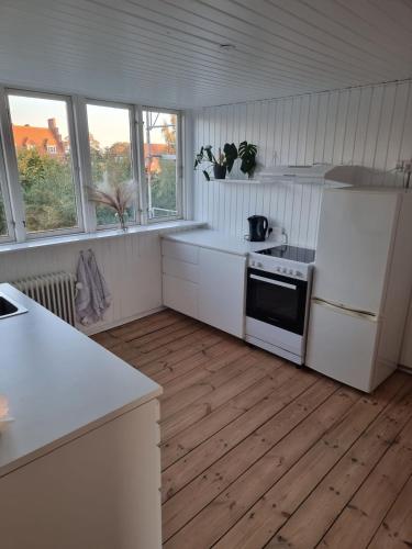 a kitchen with white appliances and wooden floors and windows at city apartment, next to the Beach in Fredericia