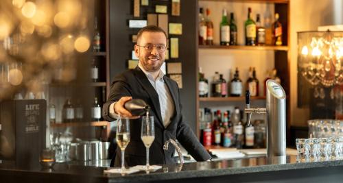a man standing at a bar with a glass of wine at Victor's Residenz-Hotel Saarlouis in Saarlouis