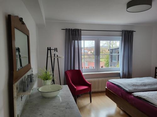 a bedroom with a bed and a red chair and a window at Ferienwohnung Kraichgaublick in Angelbachtal