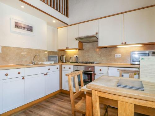 a kitchen with white cabinets and a wooden table at Cottage 2 in Keswick