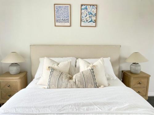a white bed with pillows and two tables with lamps at Beachfront Retreat in Falmouth