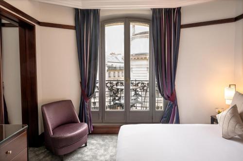a bedroom with a bed and a chair and a window at Hôtel Pont Royal Paris in Paris