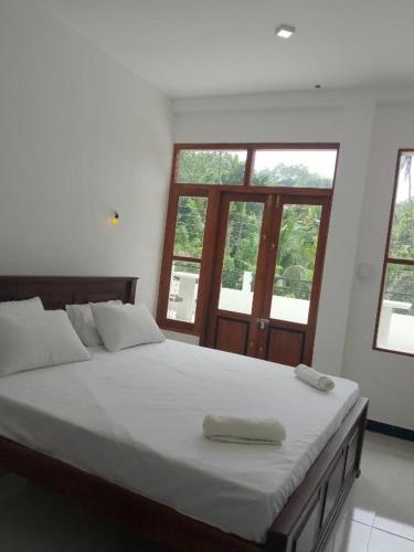 a bedroom with a large bed with white sheets and windows at Serenity villa in Weligama