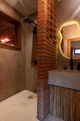 a bathroom with a brick wall and a mirror at Casa Maradi-Arena in Mazunte