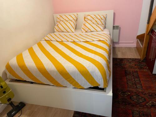 a bed with a yellow and white striped comforter at T2 accueil proche Paris in Sartrouville
