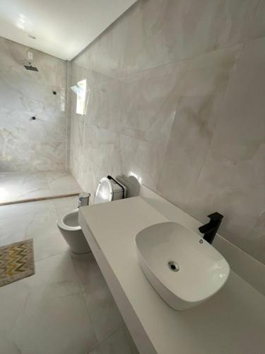 a white bathroom with a sink and a toilet at Casa Itacimirim in Camacari