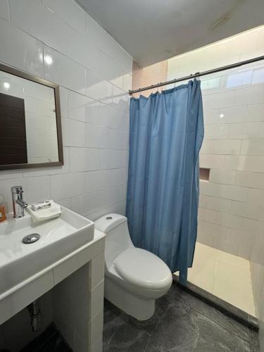 a bathroom with a toilet and a sink and a blue shower curtain at Casa Toreo in Mazatlán