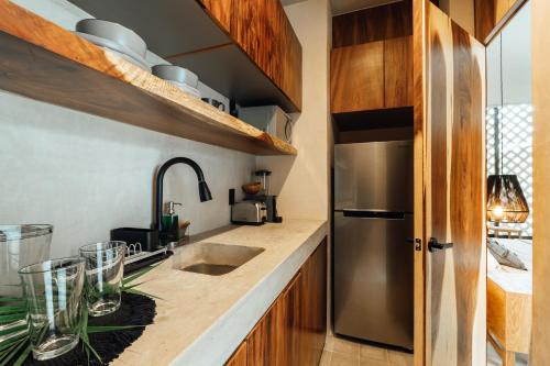 a kitchen with wooden cabinets and a stainless steel refrigerator at NAJ Boutique Hotel - Aldea Zama in Tulum