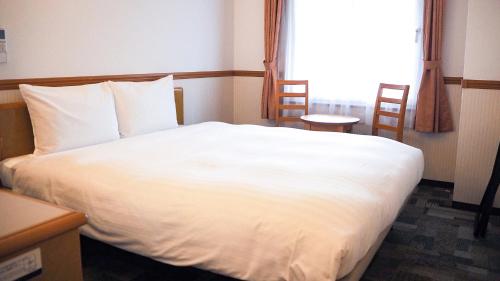 a bedroom with a white bed with two chairs and a window at Toyoko Inn Kokura-eki Minami-guchi in Kitakyushu