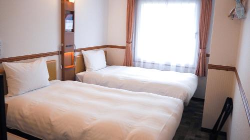 two beds in a hotel room with a window at Toyoko Inn Kokura-eki Minami-guchi in Kitakyushu