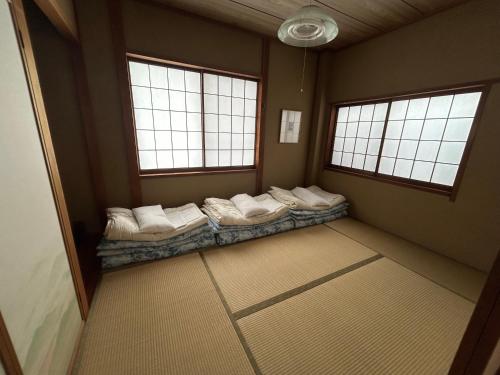 a room with a row of pillows on a bed in a room with windows at Toolate Guesthouse Toyama in Toyama
