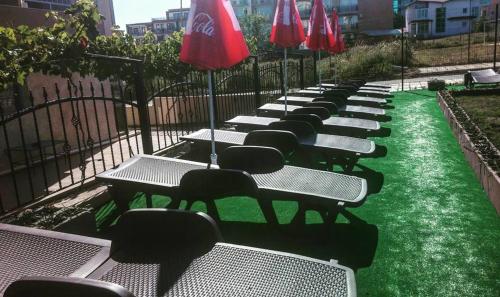 a row of picnic tables with green grass and red umbrellas at Guest House ASK in Primorsko