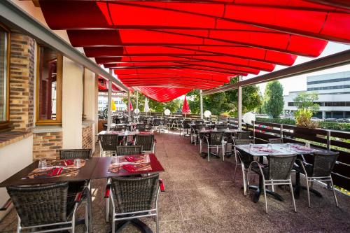 a restaurant with tables and chairs under a red umbrella at ibis Bordeaux Lac in Bordeaux