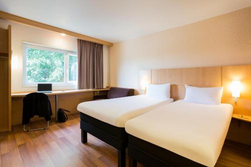 a hotel room with two beds and a desk at ibis Bordeaux Lac in Bordeaux