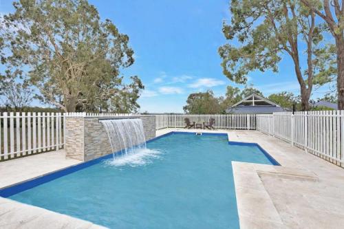 a swimming pool with a waterfall and a fence at Brokenback Homestead in Pokolbin