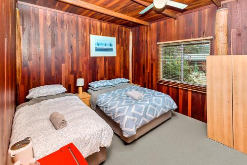 two beds in a room with wooden walls at Kin Kin Retreat in Quinninup
