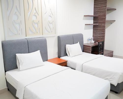two beds in a room with white sheets at Hotel Beverly Inn Batam Center in Batam Center