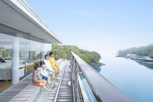 a family sitting on a balcony overlooking a river at Ooedo Onsen Monogatari Premium Toba Saichoraku in Toba