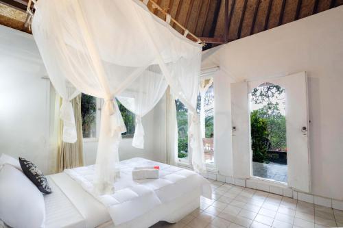 a white bed in a room with windows at Taman Indrakila in Ubud