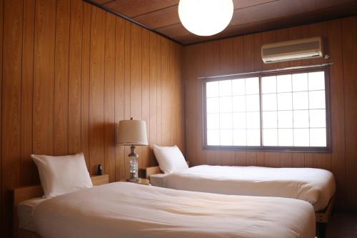 two beds in a room with wooden walls and a window at 名古屋駅 中部国際空港近くの宿ひろし in Nagoya