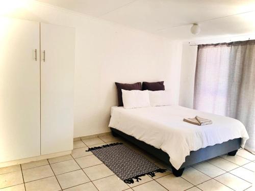 a white bedroom with a bed and a window at Alldays Sunset Lodge Wilde Street in Alldays