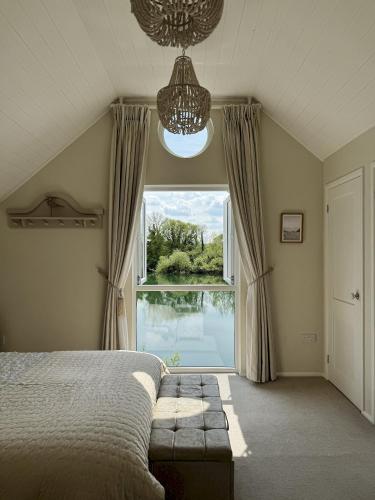 a bedroom with a bed and a large window at Peaceful Lakefront Escape w Deck Views in South Cerney