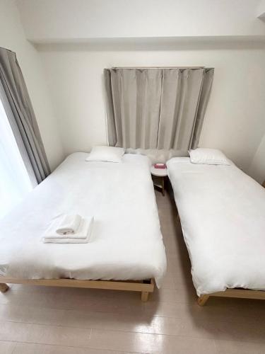 two beds in a room with white sheets and a window at 551 Namba in Osaka