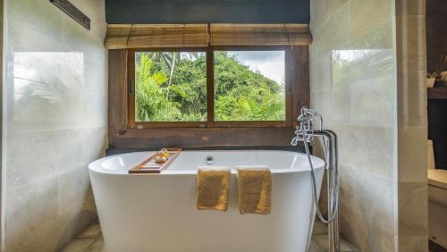 a bath tub in a bathroom with a window at The Joglo at Umah Sunset in Ubud