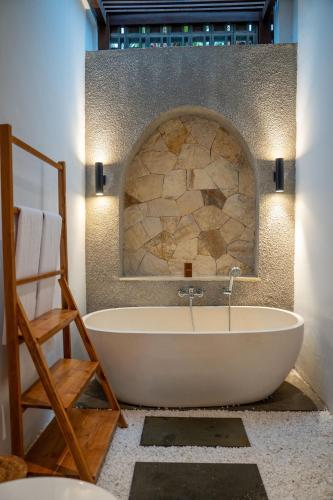 a bath tub in a bathroom with a stone wall at Yoga Sri Ubud Hotel & Spa in Ubud